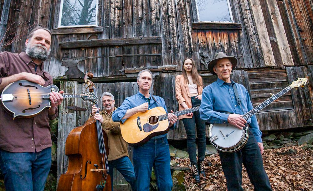 Bob and Sarah Amos band photo with bass, guitar, mandolin and banjo players outside in front of a rustic olf building