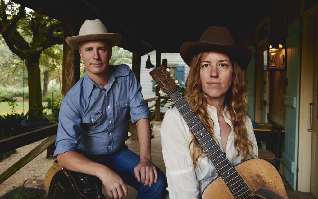 Caleb Klouder and Reeb Wilms on a rustic looking porch staring into the camera.