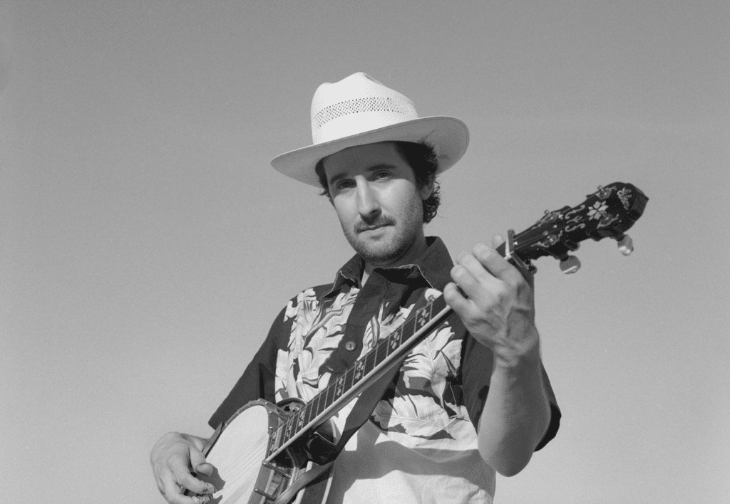 Black and white photo of banjoist,Max Wareham playing banjo, wearing a western hat and looking directly at the camera.
