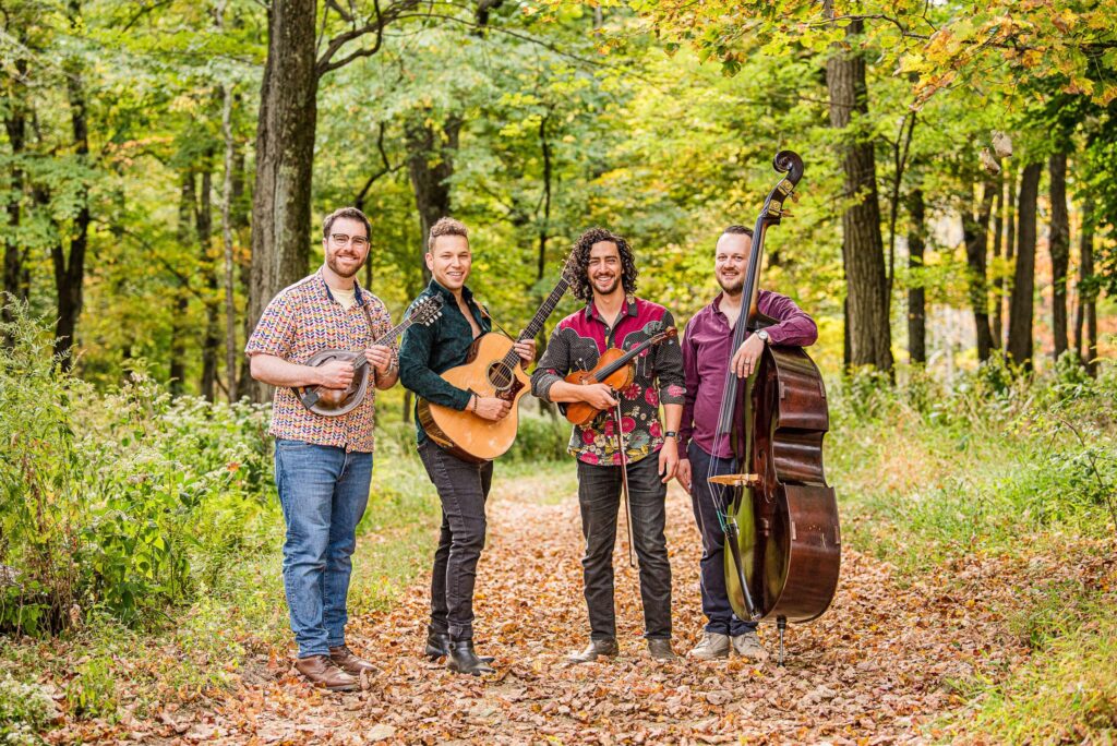 On the Trail band photo in the woods - mandolin, guitar, fiddle, and bass holding instruments